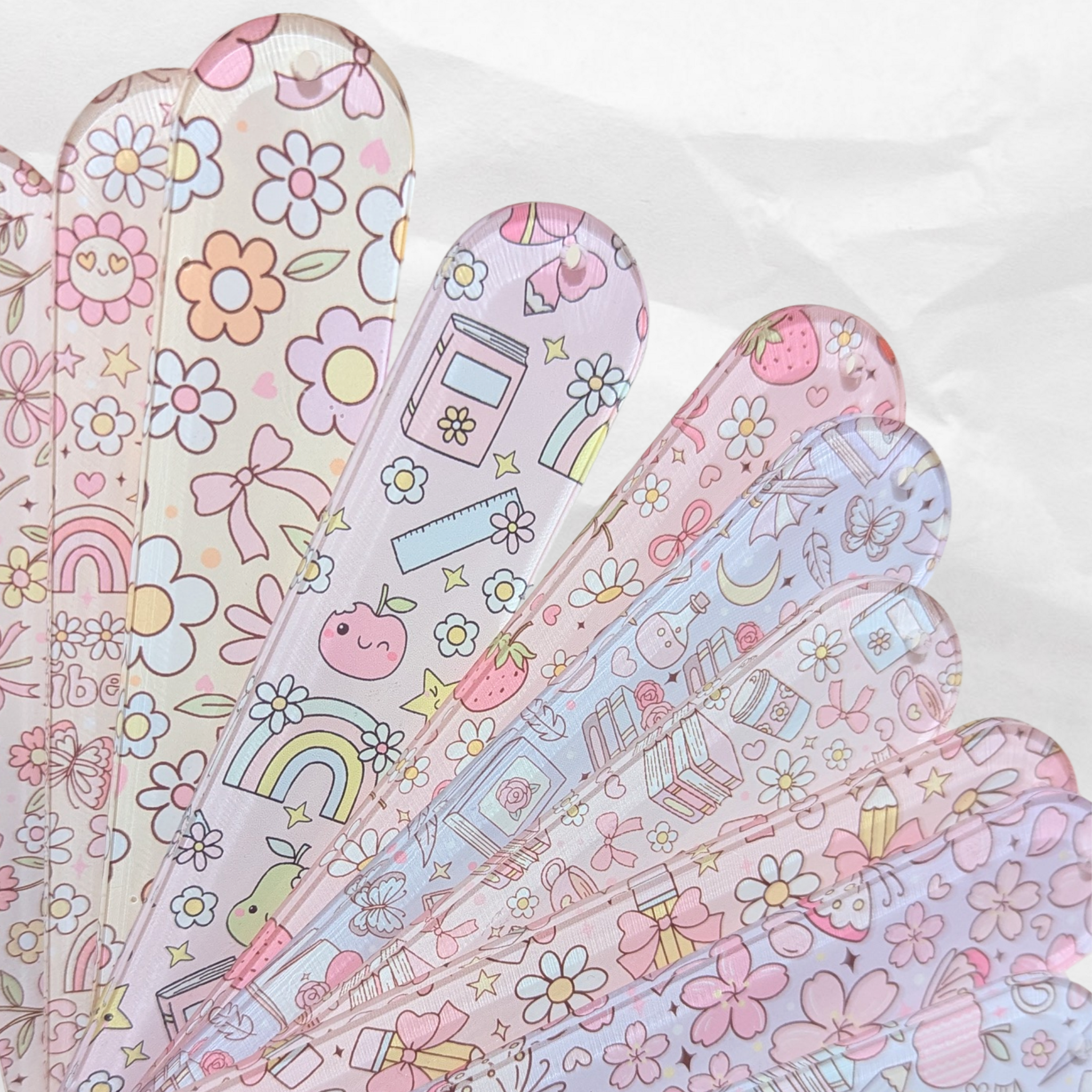 Fan of pastel acrylic bookmarks with cute patterns including flowers, books, and rainbows.