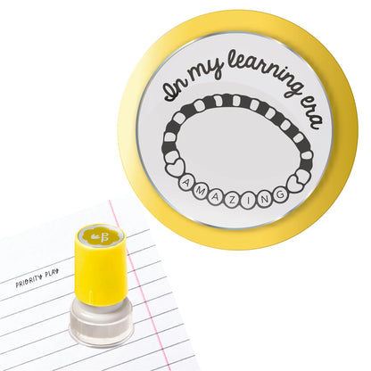 A teacher stamp showing a beaded bracelet spelling “AMAZING” with the phrase “In my learning era.”