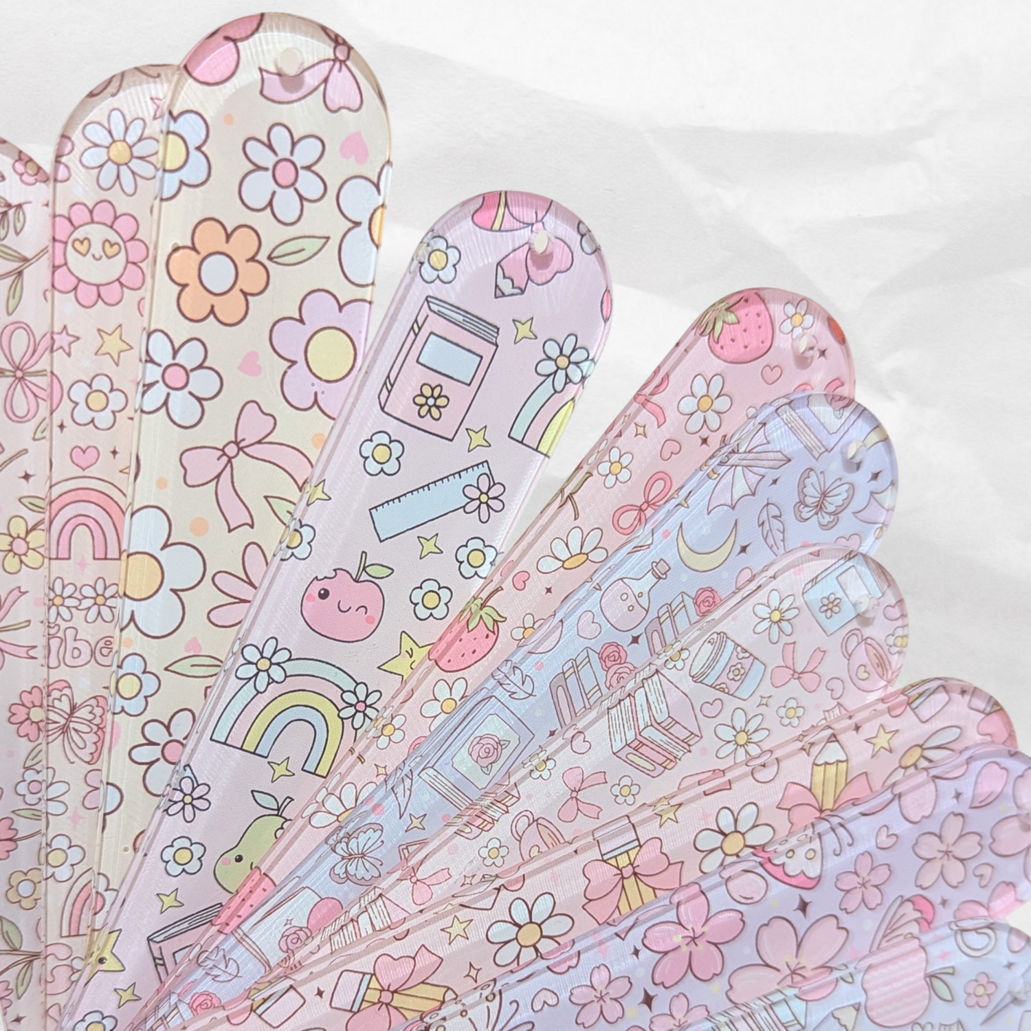 Fan of pastel acrylic bookmarks with cute patterns including flowers, books, and rainbows.
