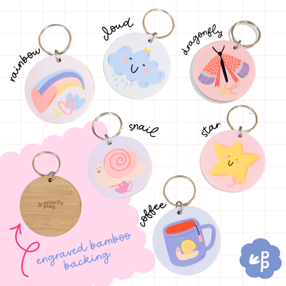 Set of pastel key tags by Priority Play showing snail, star, cloud, rainbow, coffee cup and dragonfly designs with labelled tags and engraved bamboo backing.”