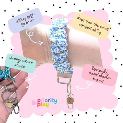 Blue floral scrunchie wristlet keychain handmade by Priority Play, shown worn on wrist with soft fabric and silver clasp, ideal for teachers or everyday use.