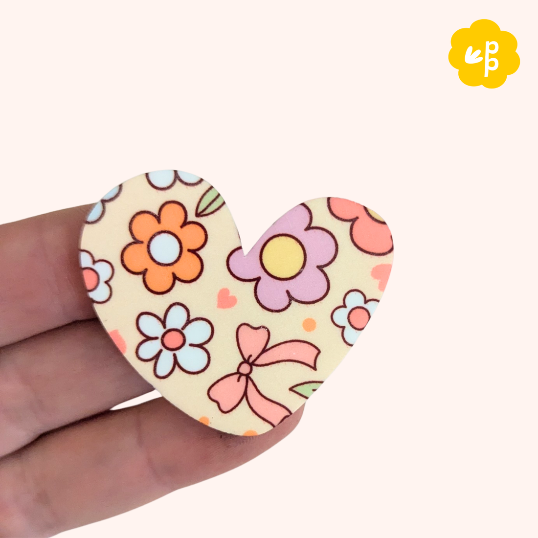 Heart-shaped floral magnet held in a hand with a white background