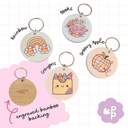 Pastel rainbow, stack of books, crayons, and groovy apple bamboo keyrings — cheerful and creative keychains ideal for teachers and students.