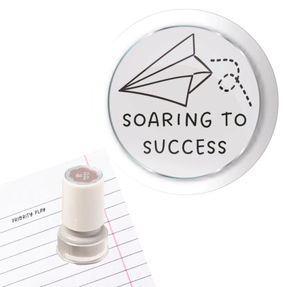 A teacher stamp showing a paper plane with a dotted trail and the message “Soaring to Success.”